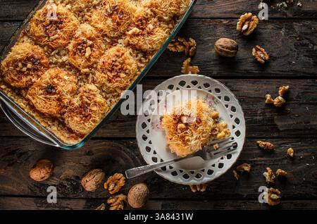 Dessert Kadaif, une pâtisserie sucrée traditionnelle du moyen-Orient et de la Méditerranée, servie sur une surface en bois foncé. Banque D'Images