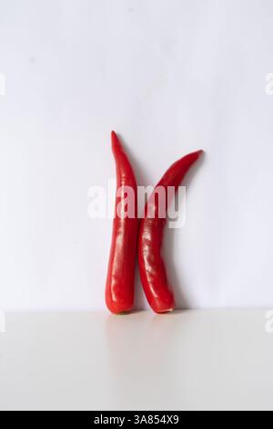 Une composition minimaliste mettant en vedette deux piments rouges éclatants debout sur un fond blanc éclatant. L'image met en évidence le b naturel Banque D'Images