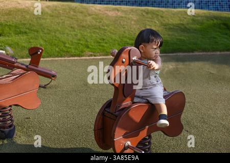 Un tout-petit est assis sur Un cheval à bascule dans le jardin, fond pour la publicité et le papier peint dans la scène relaxion et style de vie. Banque D'Images