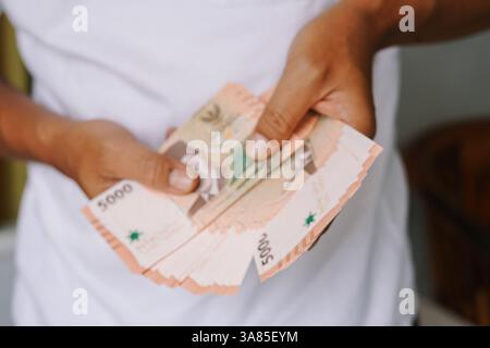 Gros plan d'une personne tenant un fan de billets de banque en roupie indonésienne. Montrant la transaction financière, le revenu, l'investissement et le concept d'économie d'entreprise Banque D'Images