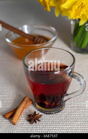 une tasse de thé aromatique avec un bol de miel et une spatule en bois, en fond avec un vase de jonquilles jaunes, avec des bâtonnets de cannelle Banque D'Images