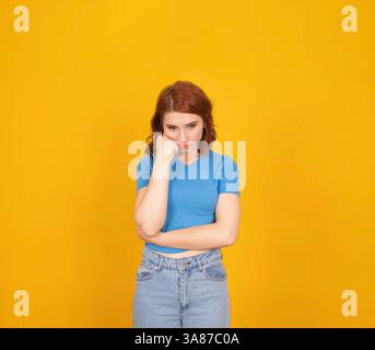 Triste femme déprimée. Porter une chemise décontractée regardant vers le bas prop vers le haut face isolé fond de studio jaune. Penser, bouleversé, solitude, rompre le concept. Banque D'Images