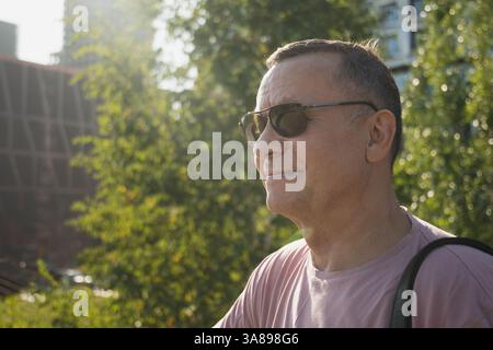 Portrait d'un homme adulte souriant portant des lunettes de soleil et un t-shirt rose au parc d'été. À l'extérieur. Gros plan. Banque D'Images