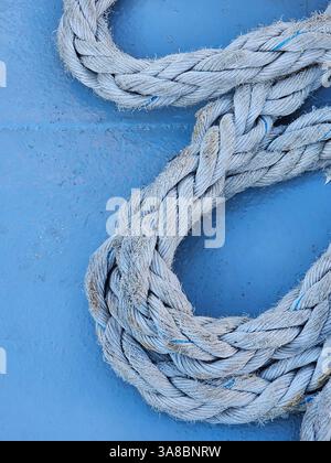 Une vue rapprochée d’une corde nautique altérée enroulée sur une surface bleue, suggérant des thèmes et des textures maritimes. Banque D'Images