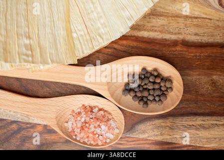 Sel de l'Himalaya et grains de poivre noir dans des cuillères en bois sur un fond rustique Banque D'Images