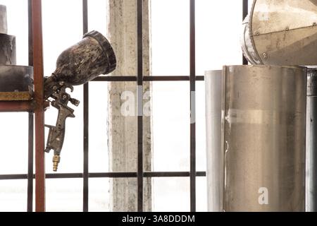 Un pistolet pulvérisateur est accroché sur une étagère dans un atelier de peintre près d'une fenêtre, le pistolet pulvérisateur est en peinture Banque D'Images