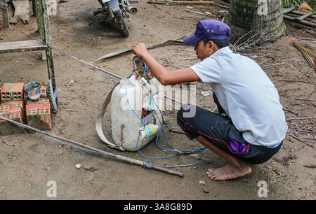 An Giang, Vietnam. 29 mars 2025. Dans la fraîcheur de l'aube, avant la chaleur de la journée, un pêcheur vietnamien prépare l'équipement pour la pêche électrique dans les rivières et ruisseaux du delta du Mékong, en utilisant une batterie de voiture dans un tambour en plastique et un onduleur haute tension fait maison fournissant un courant pulsé de l'anode à la cathode à travers l'eau. Bien que courante, cette pratique est dangereuse pour les humains et l'environnement. La pêche électrique récréative est considérée comme braconnant et interdite dans les zones d'eau douce, ainsi que toutes les méthodes destructrices d'extraction des ressources aquatiques, sauf dans les étangs domestiques. Crédit : Kevin Izorce/Alamy Live News Banque D'Images
