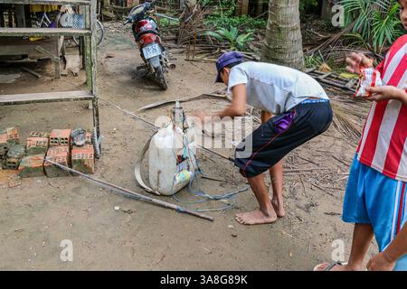 An Giang, Vietnam. 29 mars 2025. Dans la fraîcheur de l'aube, avant la chaleur de la journée, un pêcheur vietnamien prépare l'équipement pour la pêche électrique dans les rivières et ruisseaux du delta du Mékong, en utilisant une batterie de voiture dans un tambour en plastique et un onduleur haute tension fait maison fournissant un courant pulsé de l'anode à la cathode à travers l'eau. Bien que courante, cette pratique est dangereuse pour les humains et l'environnement. La pêche électrique récréative est considérée comme braconnant et interdite dans les zones d'eau douce, ainsi que toutes les méthodes destructrices d'extraction des ressources aquatiques, sauf dans les étangs domestiques. Crédit : Kevin Izorce/Alamy Live News Banque D'Images