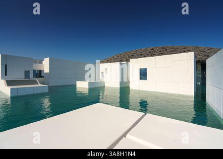 Abu Dhabi, Émirats Arabes Unis - 10 janvier 2024, vue panoramique sur la façade blanche comme neige du Louvre Abu Dhabi avec un dôme métallique entouré d'eau, Banque D'Images