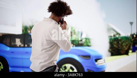 Homme afro-américain troublé parle au téléphone à côté d'une voiture fumeur. Banque D'Images