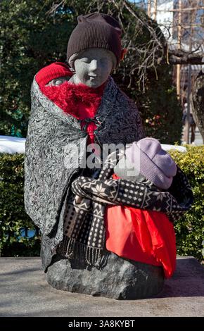 Statue en pierre de la mère et des enfants (Boshi-jizo) drapée dans une couverture, des écharpes et des bonnets en tricot vue près du temple bouddhiste Sensoji à Tokyo, au Japon Banque D'Images