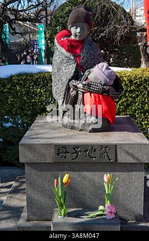 Statue en pierre de la mère et des enfants (Boshi-jizo) drapée dans une couverture, des écharpes et des bonnets en tricot vue près du temple bouddhiste Sensoji à Tokyo, au Japon Banque D'Images