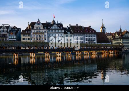 Vue sur la rivière Reuss jusqu'au pont de la Chapelle, façades d'hôtels et de maisons sur la rive de l'autre côté, au coucher du soleil. Banque D'Images
