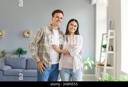 Portrait de jeune couple marié heureux debout dans le salon à la maison et serrant. Banque D'Images