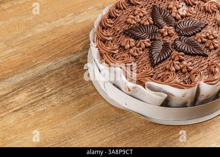 Un gâteau au chocolat magnifiquement décoré se trouve sur une base ronde, mettant en vedette des glaçures complexes et des motifs de feuilles de chocolat. La table en bois ajoute de la chaleur à Banque D'Images