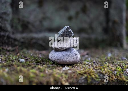 Petit empilement de trois pierres équilibrées sur une surface couverte de mousse en photo macro avec un arrière-plan flou, créant une atmosphère méditative tranquille. Banque D'Images