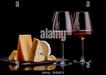 Une sélection raffinée de fromages vieillis présentés sur une planche, accompagnés d'un verre de vin, sur un fond sombre dramatique. Un cadre parfait Banque D'Images