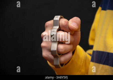 La main masculine serre les articulations en laiton métallique sur un fond noir. Concept : blessures graves et blessures, combats de rue, combats sans règles, cri urbain Banque D'Images