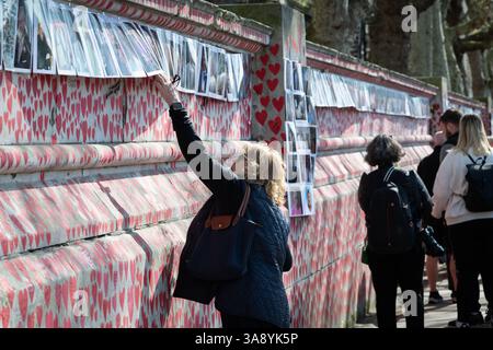 Londres, Royaume-Uni. 29 mars 2025. Les familles endeuillées et leurs proches célèbrent le quatrième anniversaire de la création du mur commémoratif national COVID sur le quai Albert, juste en face du fleuve des chambres du Parlement. L’hommage officieux s’étend sur 500 mètres avec un cœur rouge peint à la main représentant chacune des plus de 240 000 victimes de la pandémie de coronavirus au Royaume-Uni. Des centaines de photographies du défunt sont accrochées le long du mur que la procession du souvenir a marché, lisant des hommages le long du chemin. Crédit : Ron Fassbender/Alamy Live News Banque D'Images