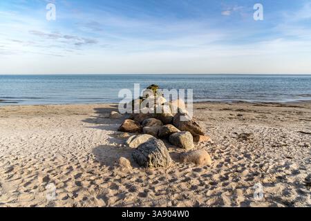 Une plage avec un gros tas de rochers dessus. Les rochers sont dispersés sur la plage, et l'eau est calme. La scène est paisible et sereine, avec le Banque D'Images