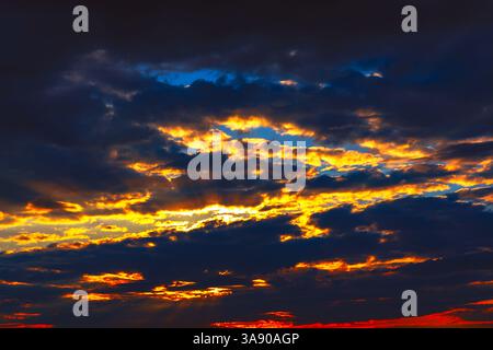 Paysages nuageux spectaculaires au coucher du soleil, teintes vibrantes d'orange et d'or sur fond sombre. Coucher de soleil ardent, avec des couleurs intenses perçant à travers la tempête Banque D'Images