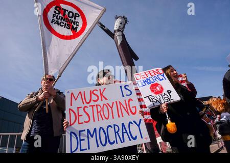 29 mars 2025, Londres, Royaume-Uni. Les manifestants contre Elon Musk et ses actions politiques dans le rassemblement américain devant le showroom de voitures Tesla à Park Royal, Londres. La manifestation de Londres fait partie d'une journée mondiale d'action sous l'égide du mouvement Tesla Takedown. Les organisateurs disent que les rassemblements auront lieu devant plus de 200 sites Tesla dans le monde. Un homme gonflable à bras ondulé représentant Elon Musk faisant un salut nazi est mis en mouvement pendant la manifestation à Londres. Banque D'Images