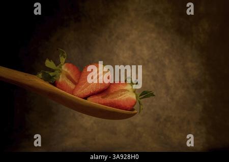 Coupez les fraises sur une cuillère en bois avec un fond sombre flou Banque D'Images