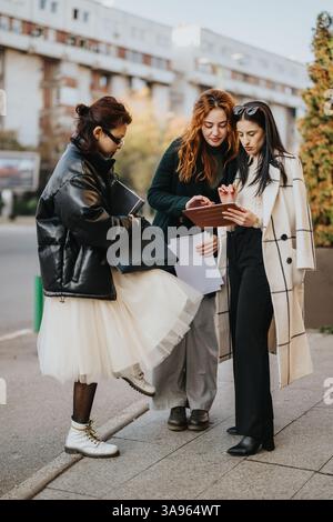 Trois femmes élégantes collaborant tout en examinant une tablette à l'extérieur par une journée ensoleillée Banque D'Images