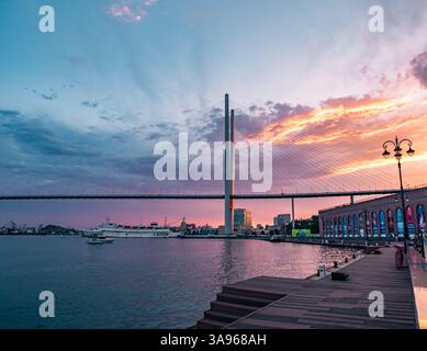 Vladivostok, Russie - 24 juin 2022 : coucher de soleil vibrant sur le Pont d'Or à Vladivostok avec des bateaux naviguant dans la baie Banque D'Images