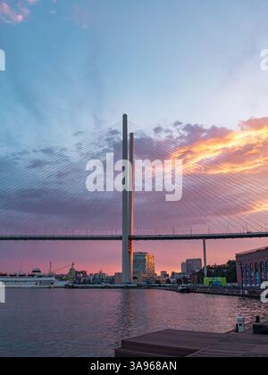 Vladivostok, Russie - 24 juin 2022 : coucher de soleil vibrant sur le Pont d'Or à Vladivostok avec des bateaux naviguant dans la baie Banque D'Images