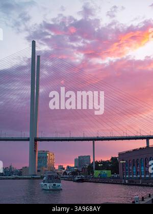 Vladivostok, Russie - 24 juin 2022 : coucher de soleil vibrant sur le Pont d'Or à Vladivostok avec des bateaux naviguant dans la baie Banque D'Images