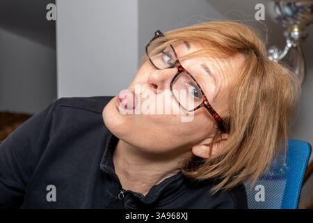 Une femme blonde avec des lunettes sort sa langue avec sa tête inclinée d'un côté Banque D'Images