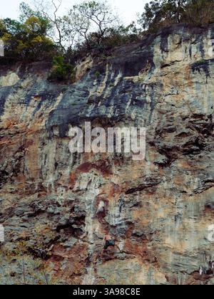 Grimpeur écaille une falaise striée de teintes minérales et de textures naturelles, éclipsée par le paysage vertical Banque D'Images