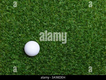 Balle de golf sur gazon artificiel. Balle de golf américaine blanche unique avec encoches spéciales, sur le côté inférieur gauche d'une surface plate en plastique en herbe. Banque D'Images