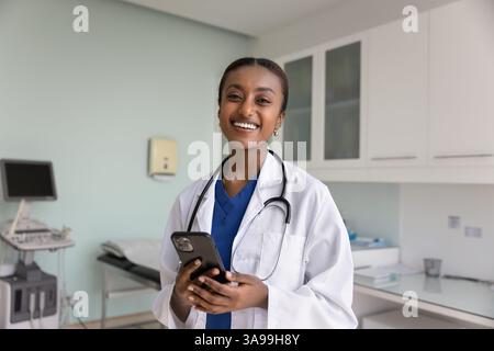 Heureuse belle femme médecin africaine tenant smartphone Banque D'Images