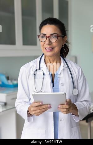 Femme médecin d'âge moyen positive dans des lunettes tenant un comprimé Banque D'Images