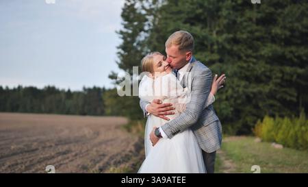 Jeunes mariés romantiques partageant un baiser passionné, embrassant au milieu d'une végétation luxuriante avec un fond boisé symbolisant l'intimité du jour du mariage Banque D'Images