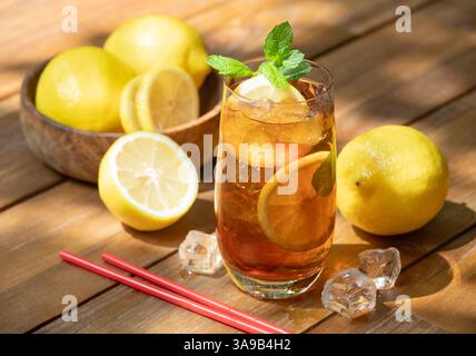 Verre de thé glacé avec des tranches de citron et de menthe et citrons frais à l'extérieur sur une table en bois Banque D'Images