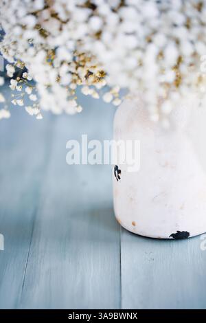 Bouquet de fleurs de souffle de bébé dans un vase blanc rustique sur une table bleue pour la fête des mères. Mise au point sélective avec arrière-plan extrêmement flou. Banque D'Images