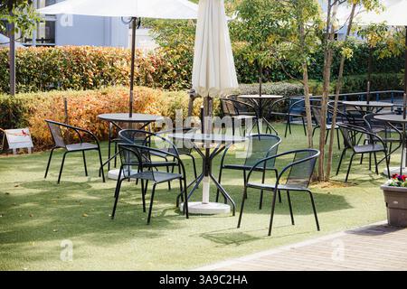 Table extérieure et ensemble de chaises, espace salon du restaurant ou du café dans la zone d'herbe verte du parc public pour les bains de soleil chauds. Banque D'Images