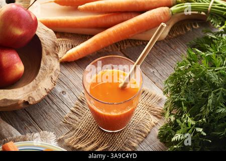 Un verre de jus de carotte frais avec paille de bambou écologique et pommes rouges Banque D'Images