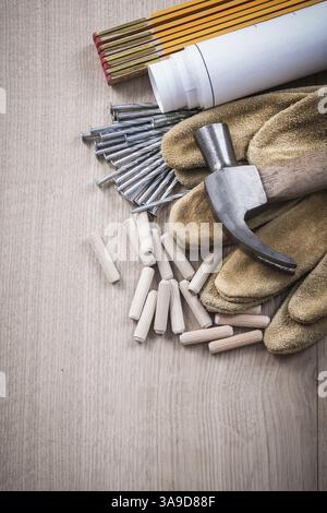 Chevilles de compteur en bois blueprints griffe marteau paire de gants de sécurité et clous en métal sur le concept de construction de panneau de bois Banque D'Images