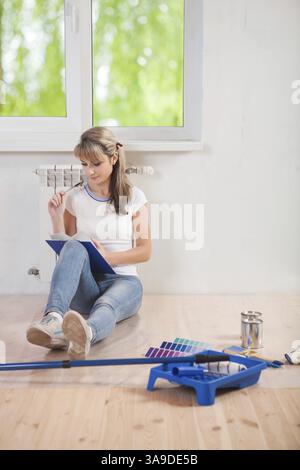 Belle femme assise sur le sol. regarder dans le presse-papiers et penser Banque D'Images