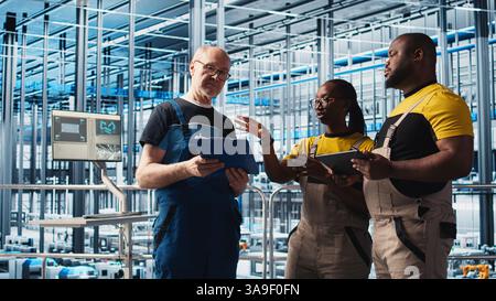 L'ingénieur principal de l'usine photovoltaïque d'industrie 4,0 lisant la paperasse discute avec les travailleurs pour maximiser la production d'énergie. Panneaux solaires SMART usine leader expérimenté donnant des tâches aux techniciens, caméra A. Banque D'Images
