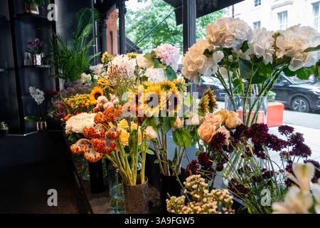 Des fleurs colorées dans des vases et des bouquets sont disposées soigneusement à l'intérieur d'une boutique de fleuriste. La lumière naturelle et la variété des fleurs créent un atmo frais et élégant Banque D'Images