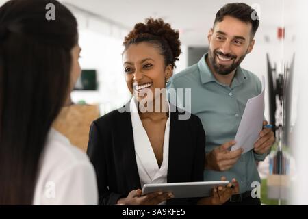 Partenaires commerciaux heureux et diversifiés discutant au tableau blanc, discutant de la collaboration Banque D'Images
