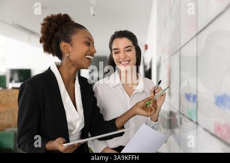 Heureuses collègues d'affaires féminines diverses travaillant sur la planche à roulettes Kanban Banque D'Images