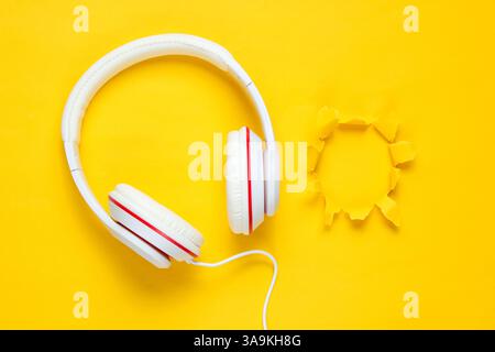 Casque filaire blanc classique sur fond de papier jaune violet avec trou déchiré. Style rétro. 80s. Culture pop. Vue de dessus. Concept musical minimal Banque D'Images