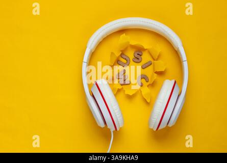 Casque filaire blanc classique sur fond de papier jaune avec trou déchiré. Style rétro. 80s. Culture pop. Vue de dessus. Musique de mot Banque D'Images