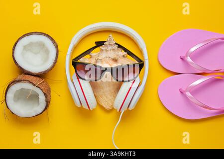 Fond de plage d'été créatif. Vacances à la plage. Écouteurs, lunettes de soleil, noix de coco, coquille, flip flop sur fond jaune. Vue de dessus. Pose à plat Banque D'Images
